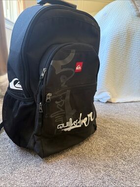 Quicksilver  Black Backpack / luggage  
on wheels with White Logo and Red Patch